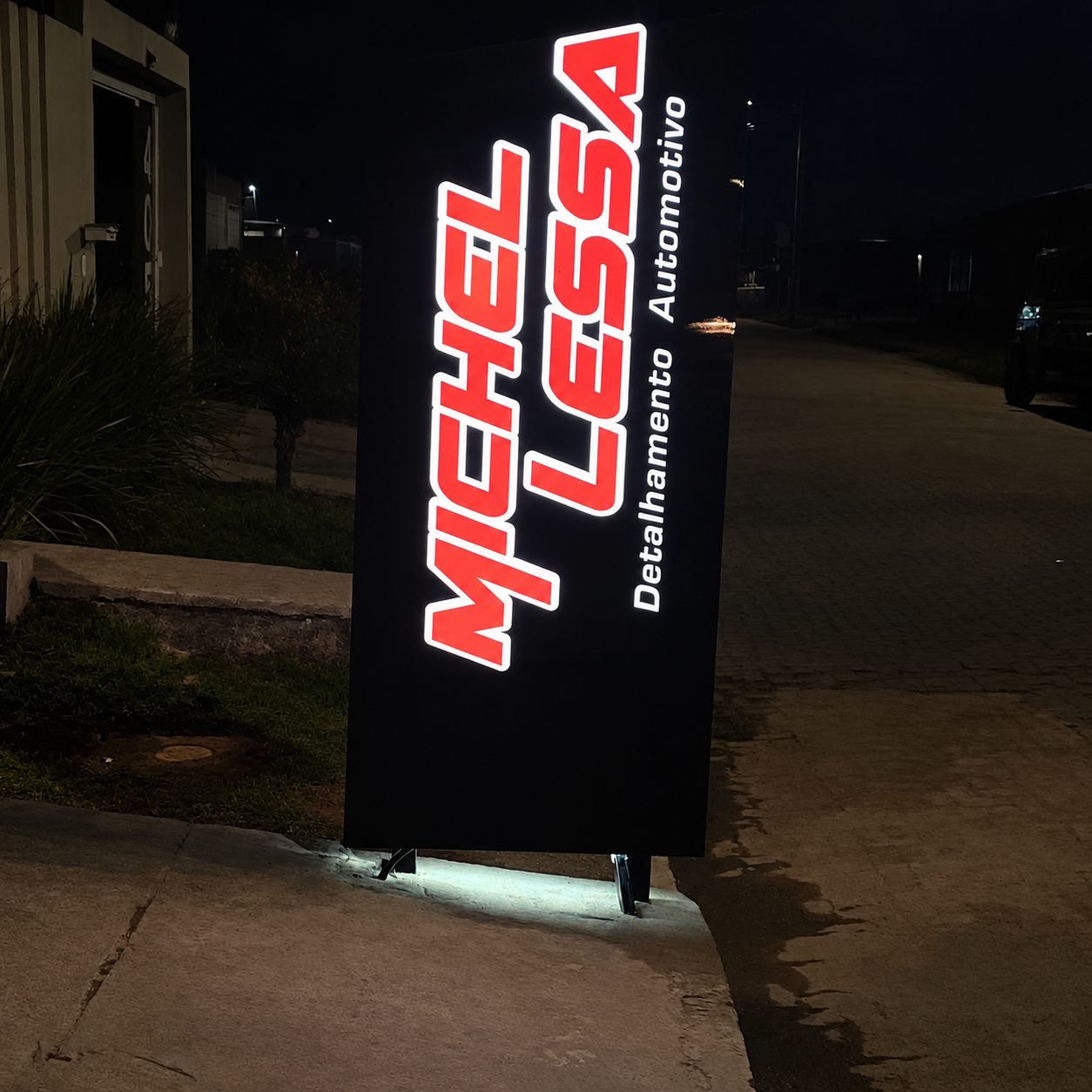 Totem luminoso com logotipo em LED vermelho e branco aceso à noite